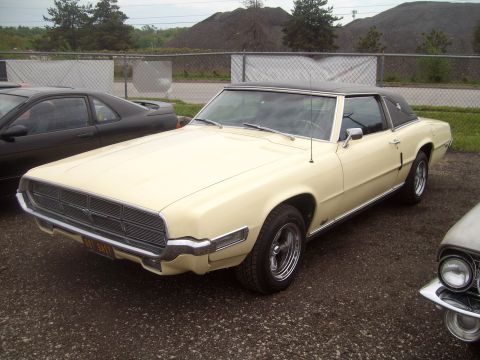 2004 Ford Crown Victoria - A cream-colored coupe, likely from the 1970s, is parked next to another vehicle under an overcast sky.