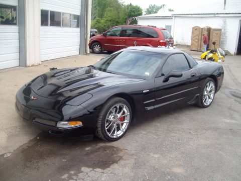 2004 Ford Crown Victoria - A black Chevrolet Corvette C5 is parked outside a garage with a red minivan in the background.