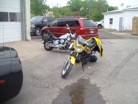 2004 Ford Crown Victoria - Two motorcycles are parked outside a garage, with other vehicles in the background.