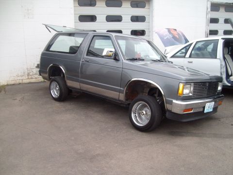 2004 Ford Crown Victoria - This gray SUV features custom chrome wheels and a lifted rear end, parked in front of a garage with another vehicle nearby.