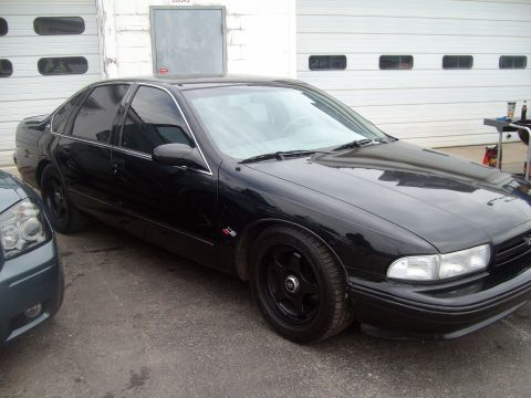 2004 Ford Crown Victoria - Black sedan with aftermarket wheels parked outside a garage.