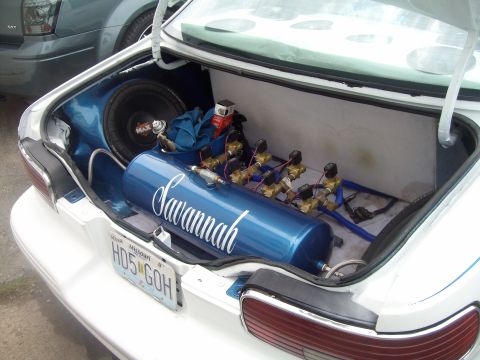 2004 Ford Crown Victoria - The trunk of a car is modified with a custom air suspension system and a subwoofer, with another vehicle partially visible.