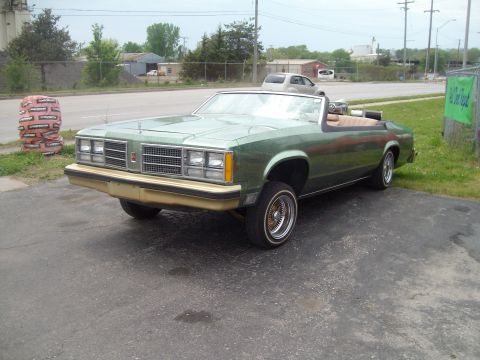 2004 Ford Crown Victoria - A green convertible with a tan interior is parked on asphalt with a grassy area and buildings in the background.