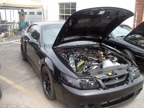 2004 Ford Crown Victoria - A black Ford Mustang is parked with its hood open, revealing the engine bay. Another car is visible behind it.