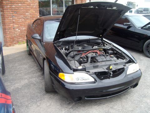 2004 Ford Crown Victoria - A black Ford Mustang is parked outside a building with its hood open, revealing the engine compartment.