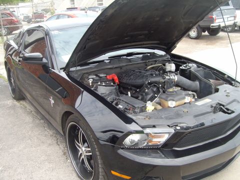 2004 Ford Crown Victoria - The engine bay of a black Ford Mustang is visible with the hood raised, revealing custom wheels and aftermarket parts.