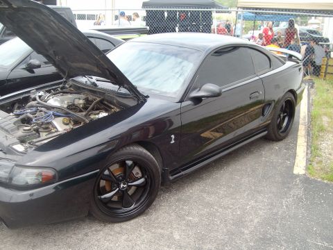 2004 Ford Crown Victoria - Black 1996 Ford Mustang Cobra parked with its hood open, revealing the engine bay.