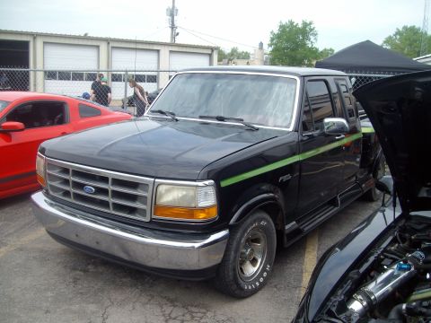 2004 Ford Crown Victoria - A black Ford F-150 pickup truck is parked outside a building with a red sports car and another vehicle with its hood open.