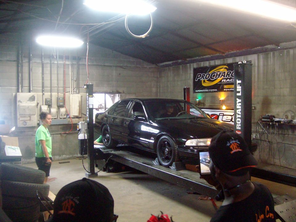 Black sedan on a rotary lift in a garage with people watching