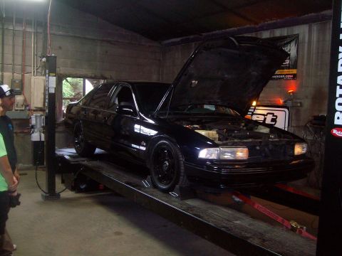 2004 Ford Crown Victoria - A black sedan is positioned on a car lift with its hood open, showing the engine bay.