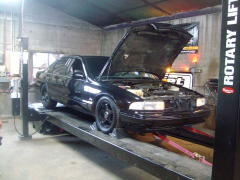2004 Ford Crown Victoria - A black sedan is positioned on a car lift with its hood open, revealing the engine bay.