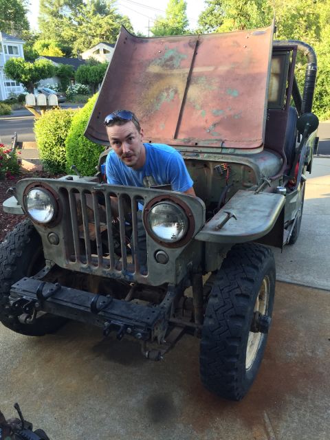 1946 Jeep Willys - Man works on a 1946 Jeep CJ5, hood open, revealing the engine bay.