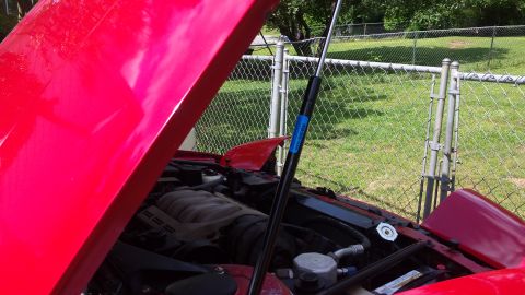 1991 Buick Reatta - Engine bay of a red car with the hood propped open, revealing the engine and various components.