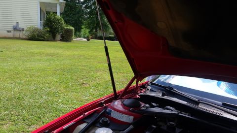 1991 Buick Reatta - View of a car's engine compartment with the hood raised, set against a backdrop of a residential lawn.