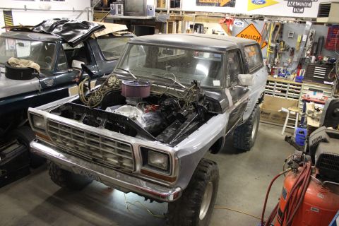 1979 Ford Bronco - A Ford Bronco is in a garage with its hood open, revealing the engine, with another vehicle partially visible behind it.