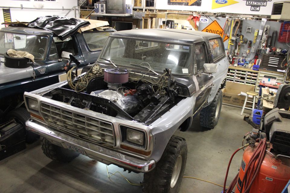 Gray and black Ford Bronco in a garage, hood open, engine exposed, front view