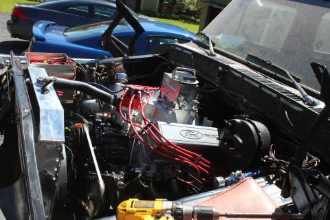 1979 Ford Bronco - Close-up of a modified Ford V8 engine, with other vehicles parked behind it.