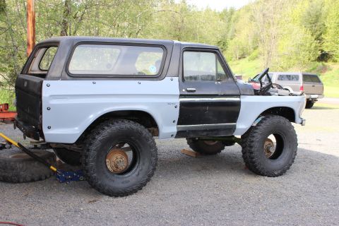 1979 Ford Bronco - Ford Bronco in gray primer and black, raised on stands with tires and parts beside it during a rebuild.