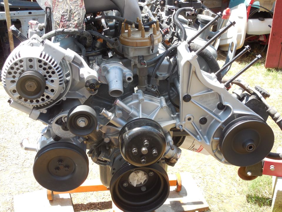 Rebuilt silver V8 engine on a pallet showing alternator, pulleys and distributor
