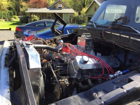 1979 Ford Bronco - The engine compartment of a truck is shown, a V8 engine with custom parts and wiring. Another vehicle is visible in the background.