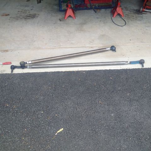 1978 Ford Bronco - Two tie rods are laid out on asphalt, with red jack stands visible in the background.