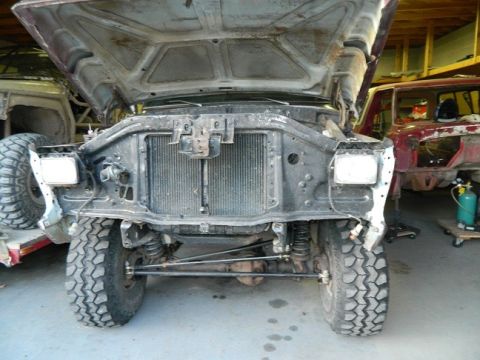 1979 Ford Bronco - This Ford Bronco is in a workshop, with its hood up and front end disassembled. Another vehicle is parked behind it.