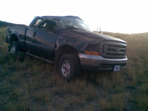 1979 Ford Bronco - This heavily damaged black Ford F-350 pickup truck sits in a grassy field, its roof and front end severely compromised.
