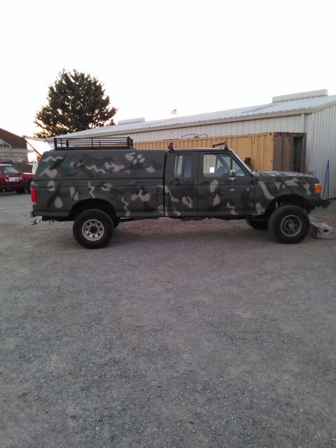 1991 Ford Bronco - Side view of a camouflaged Ford F-250 crew cab pickup with a camper shell and roof rack.