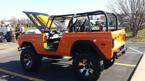 1995 Ford Bronco - This orange Ford Bronco features a roll cage, aftermarket wheels, and the hood is open, revealing "Ford 302" engine text.