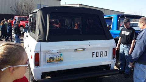 1995 Ford Bronco - White Ford Bronco with a black soft top is parked outdoors, with other vehicles and people nearby.