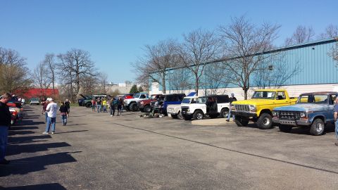 1995 Ford Bronco - A collection of Ford Broncos and trucks are gathered in a parking lot under a clear blue sky.