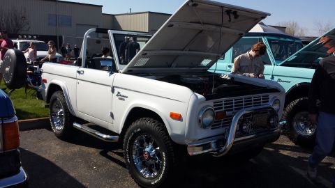 1995 Ford Bronco - White Ford Bronco convertible with hood open, parked next to a light blue Ford Bronco at an outdoor event.
