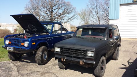 1995 Ford Bronco - Two Ford Broncos, one blue with its hood up and one black, are parked side-by-side outdoors.