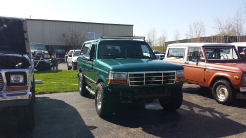 1995 Ford Bronco - A green 1995 Ford Bronco is parked in front of a building, with another Bronco visible to its right.