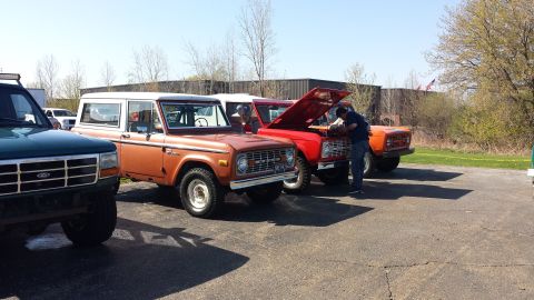 1995 Ford Bronco - Several Ford Broncos are parked outside on a sunny day, with one person attending to the engine of a red Bronco.