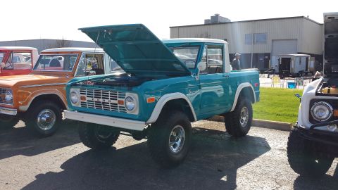 1995 Ford Bronco - A teal Ford Bronco is parked with its hood open, alongside other Broncos.