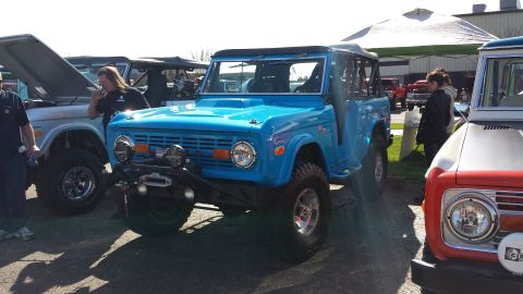 1995 Ford Bronco - A bright blue first-generation Ford Bronco is parked at an outdoor event with other vehicles.