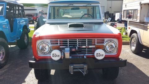 1995 Ford Bronco - This classic Ford Bronco features a prominent grille, winch, and auxiliary lights, with other vehicles visible in the background.