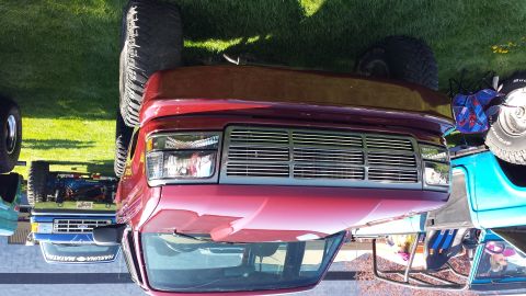 1995 Ford Bronco - Front view of a red SUV with a prominent chrome grille, parked outdoors with other vehicles.