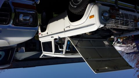 1995 Ford Bronco - White 1978 Ford Bronco, hood ajar, parked alongside another vehicle. The grille and headlights are visible.