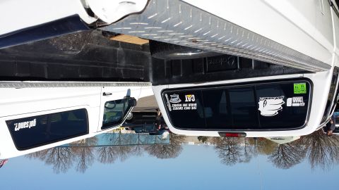 1995 Ford Bronco - A white pickup truck is viewed from the rear, showing its bed and tinted windows with various stickers.