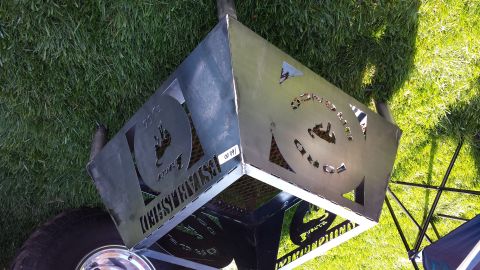 1995 Ford Bronco - A metal fire pit with decorative cutouts sits on grass next to a tire and a SuperMotors logo.