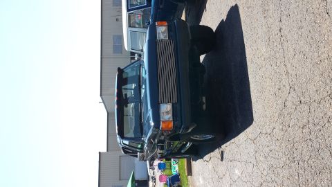 1995 Ford Bronco - A dark blue pickup truck is parked next to another vehicle, showing its front grille and headlights.