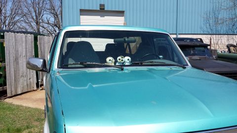 1995 Ford Bronco - Teal SUV parked outdoors with stuffed animals on the dashboard. Another vehicle is visible in the background.