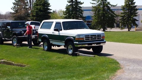 1995 Ford Bronco - A white and green Ford Bronco is parked next to a black Jeep.