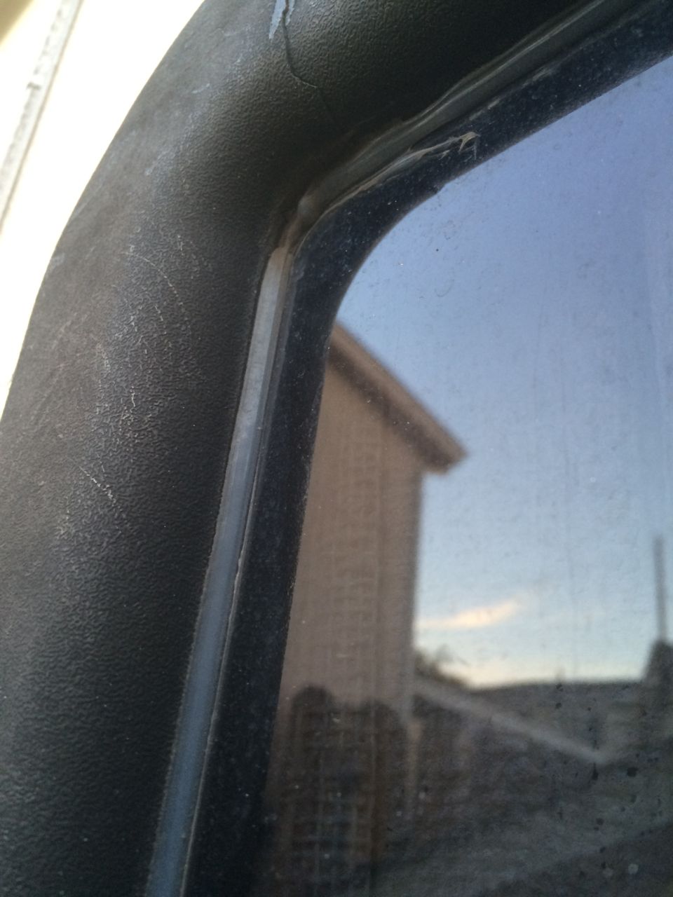 Close-up of a black textured door frame and window seal, with a reflection of a building in the glass