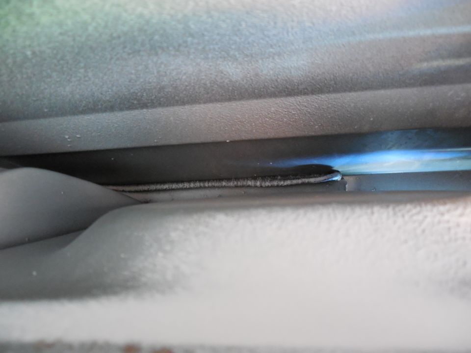 Tight underbody view of white-coated panels and sealed inner flange with light through the gap