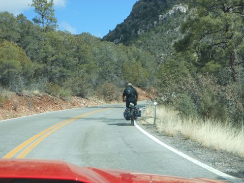 1995 Ford Bronco - View from inside a red vehicle shows a cyclist on a winding road through a mountainous, wooded area.