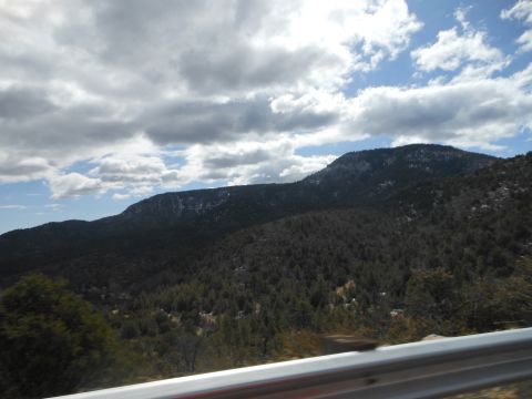 1995 Ford Bronco - A view of a forested mountain range under a dramatic sky, as seen from a moving vehicle.