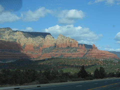 1995 Ford Bronco - A scenic view of red rock formations and lush green trees under a bright blue sky with scattered clouds. The Supermotors.net logo is visibl…
